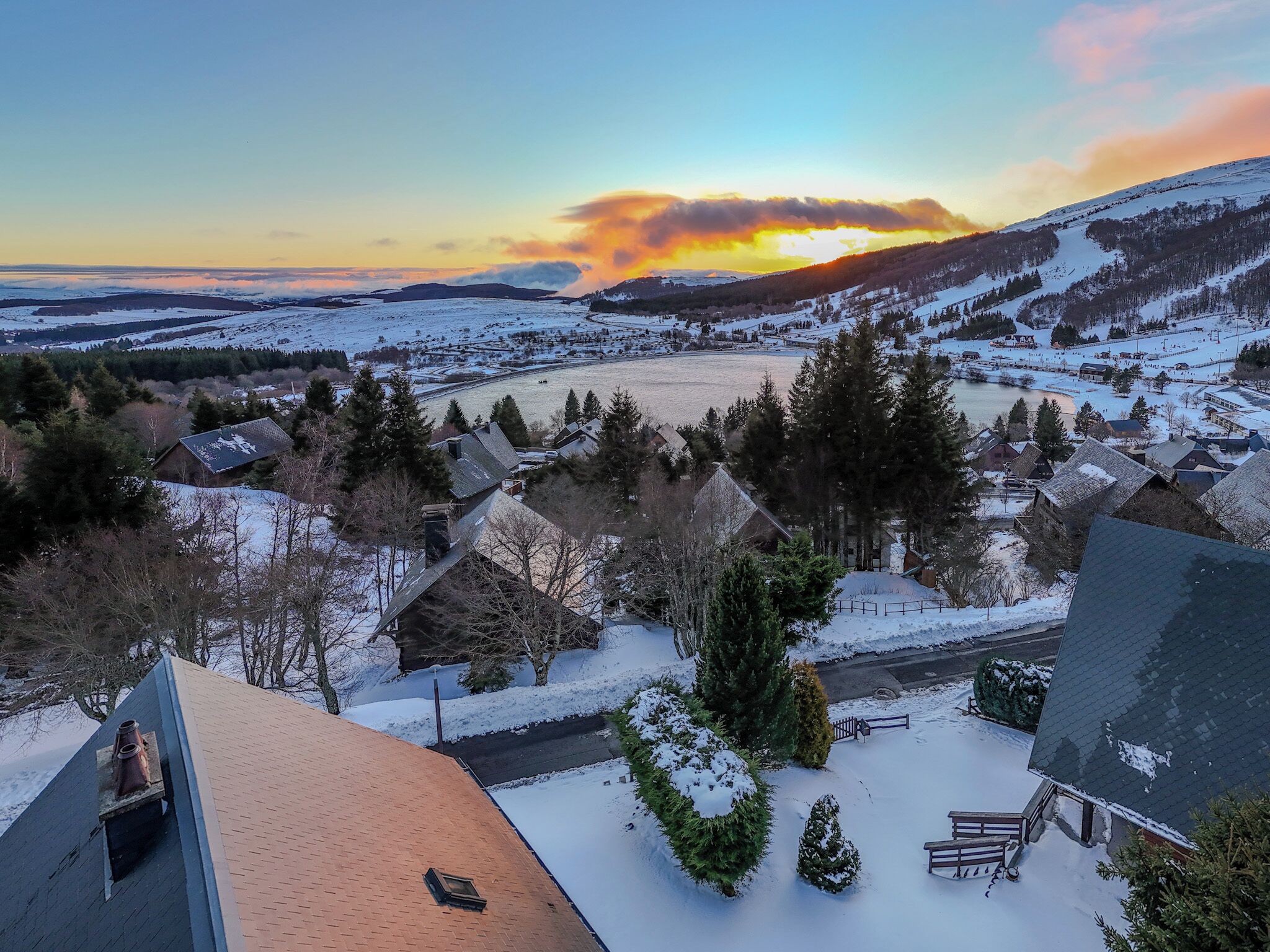 Un pueblo cubierto de nieve con casas tradicionales, un río y una puesta de sol al fondo.