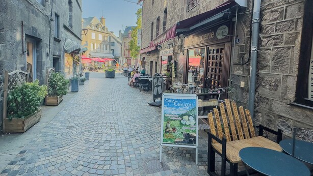 Een straat met keien, terrasjes en een bord voor een lokaal restaurant.