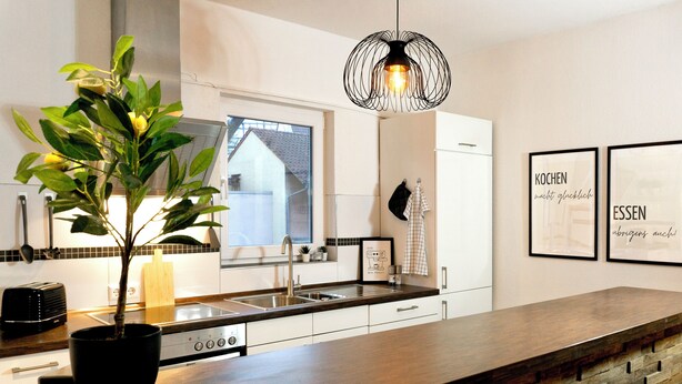 A modern kitchen with a wooden countertop, a built-in stove, and a hanging light fixture. - Turmstube - 110 m² design apartment in Kürnbach, Auszeitapartments (Kürnbach)