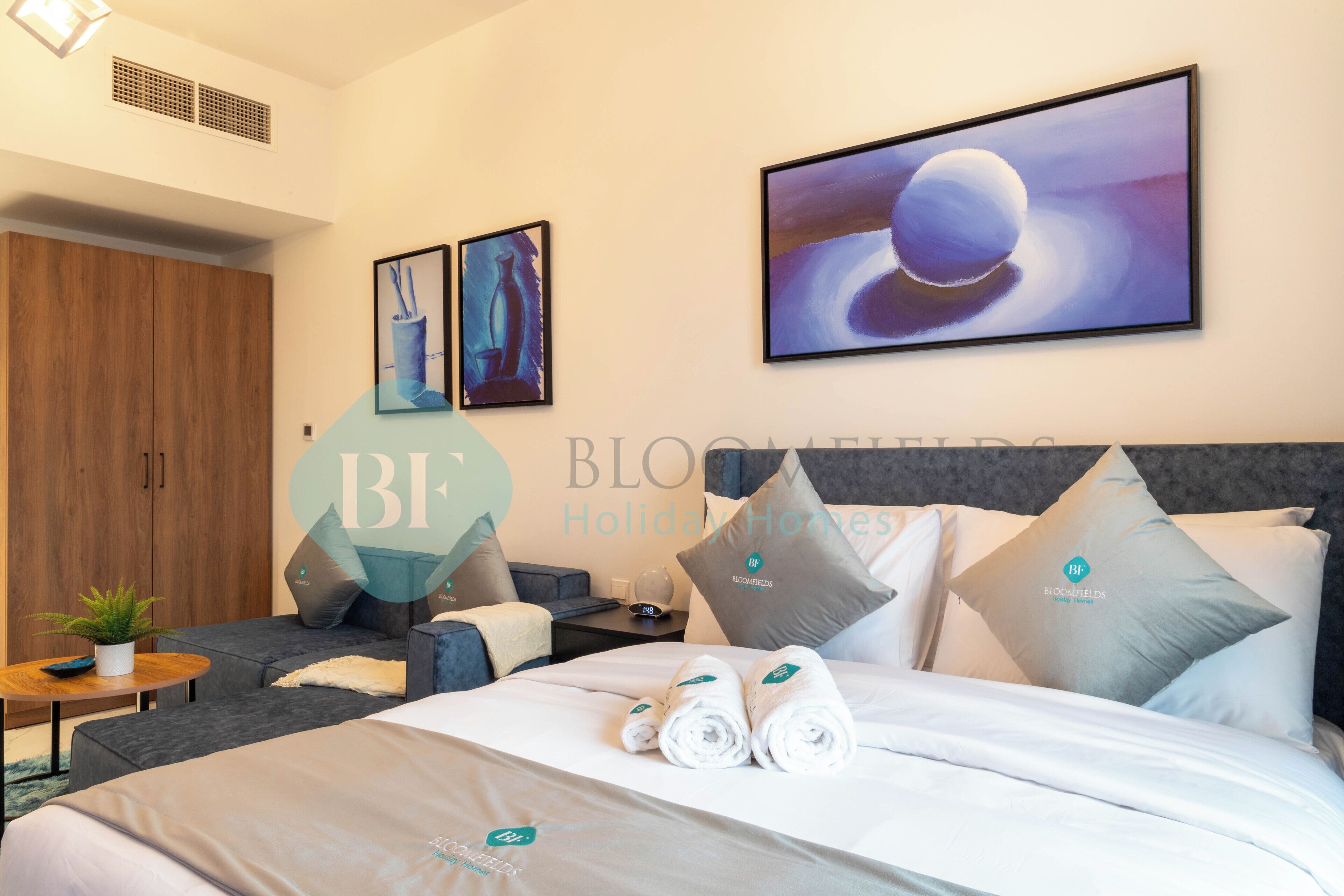 A hotel room with a bed, a sofa, a nightstand, and a wall with artwork.