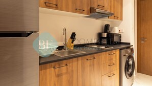 A modern kitchen with wooden cabinets, a stainless steel sink, a coffee maker, and a washing machine. - Bloomfields Spectacular STU in Oasis (Abu Dhabi)