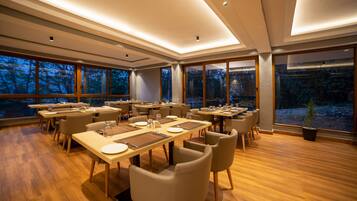 Un comedor moderno con varias mesas y sillas, ventanas amplias que ofrecen vistas al exterior, y suelo de madera.