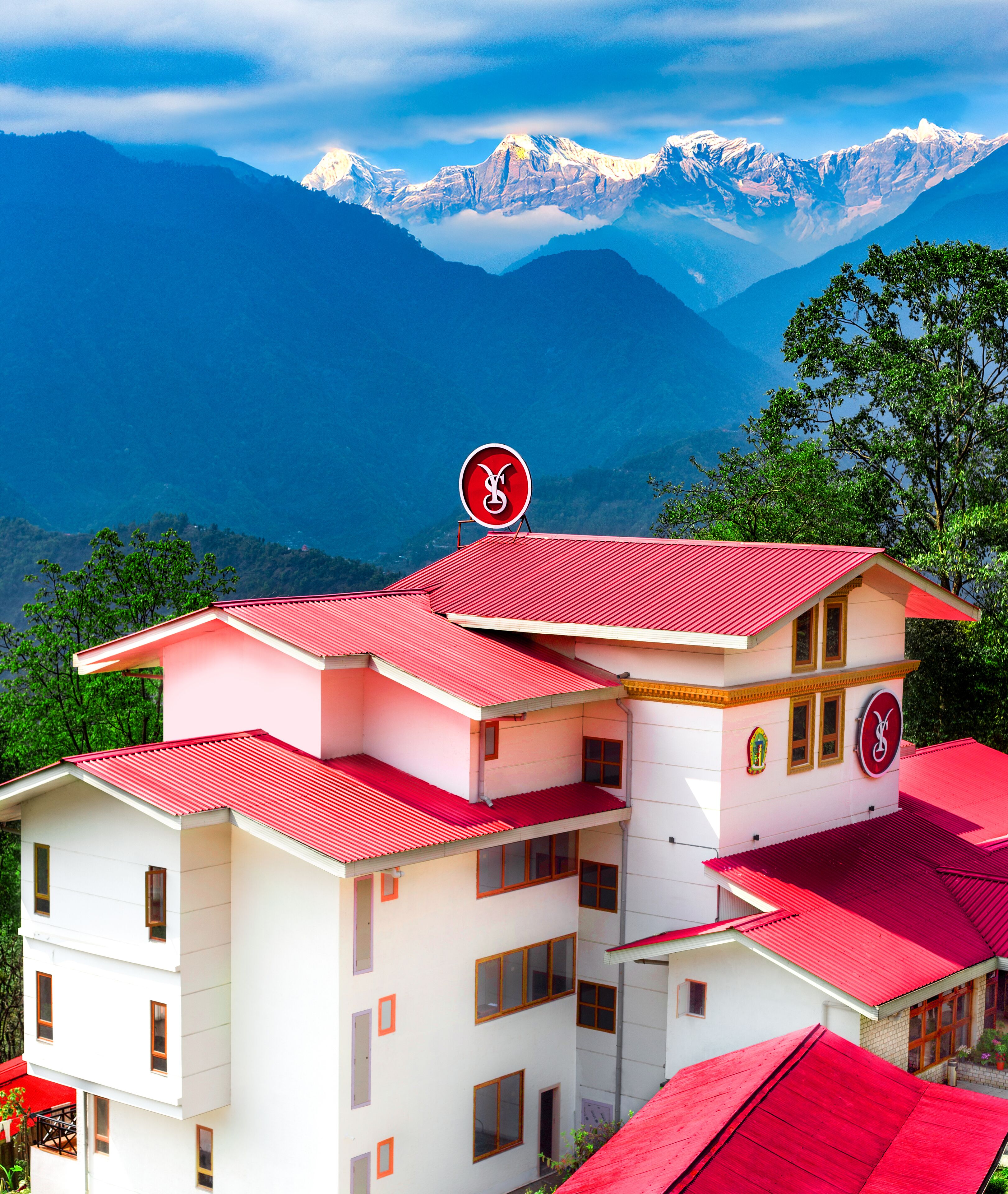 A multi-story building with a red roof, white walls, and a mountain view.