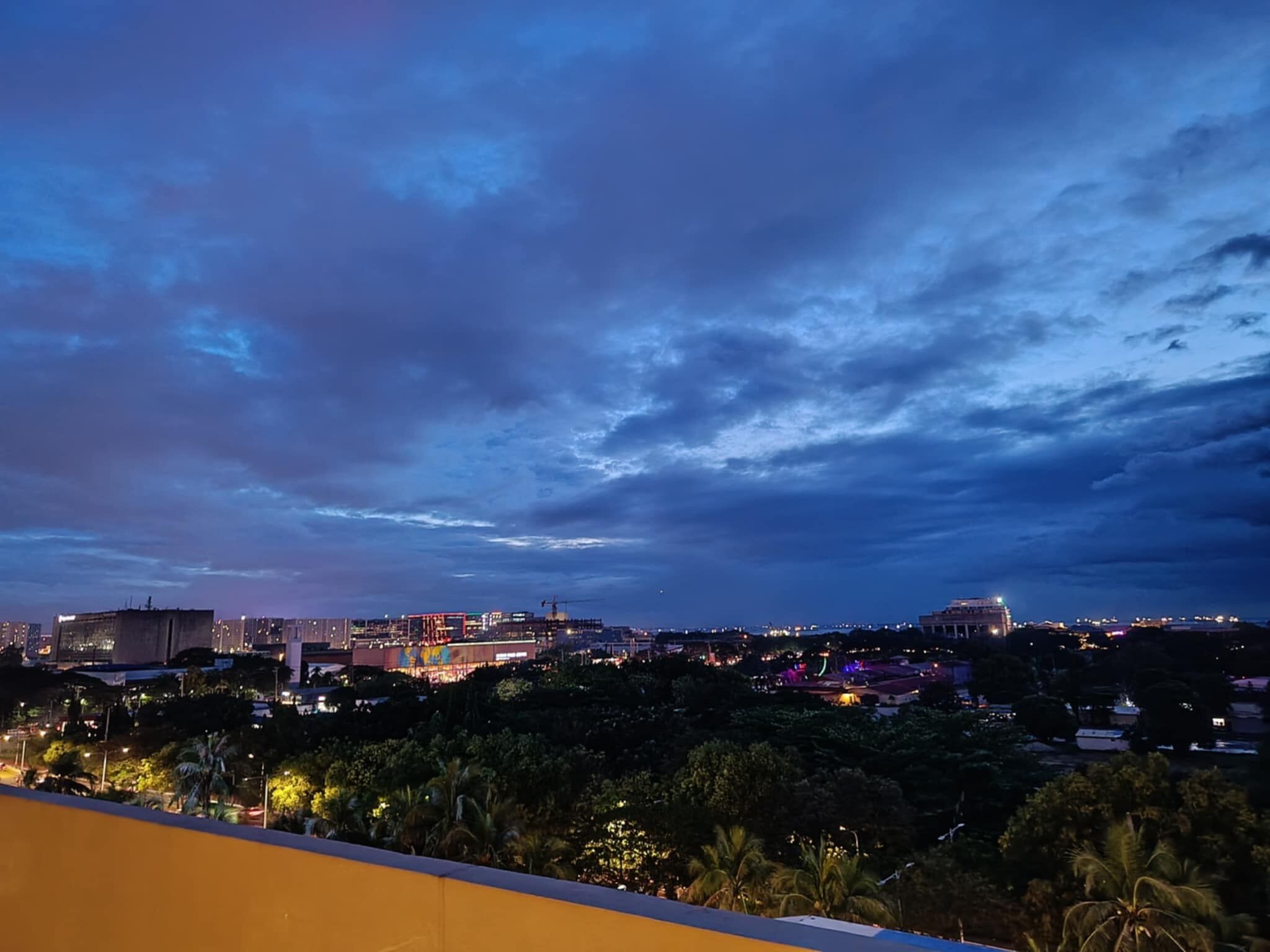 A cityscape at dusk with buildings, a stadium, and palm trees.