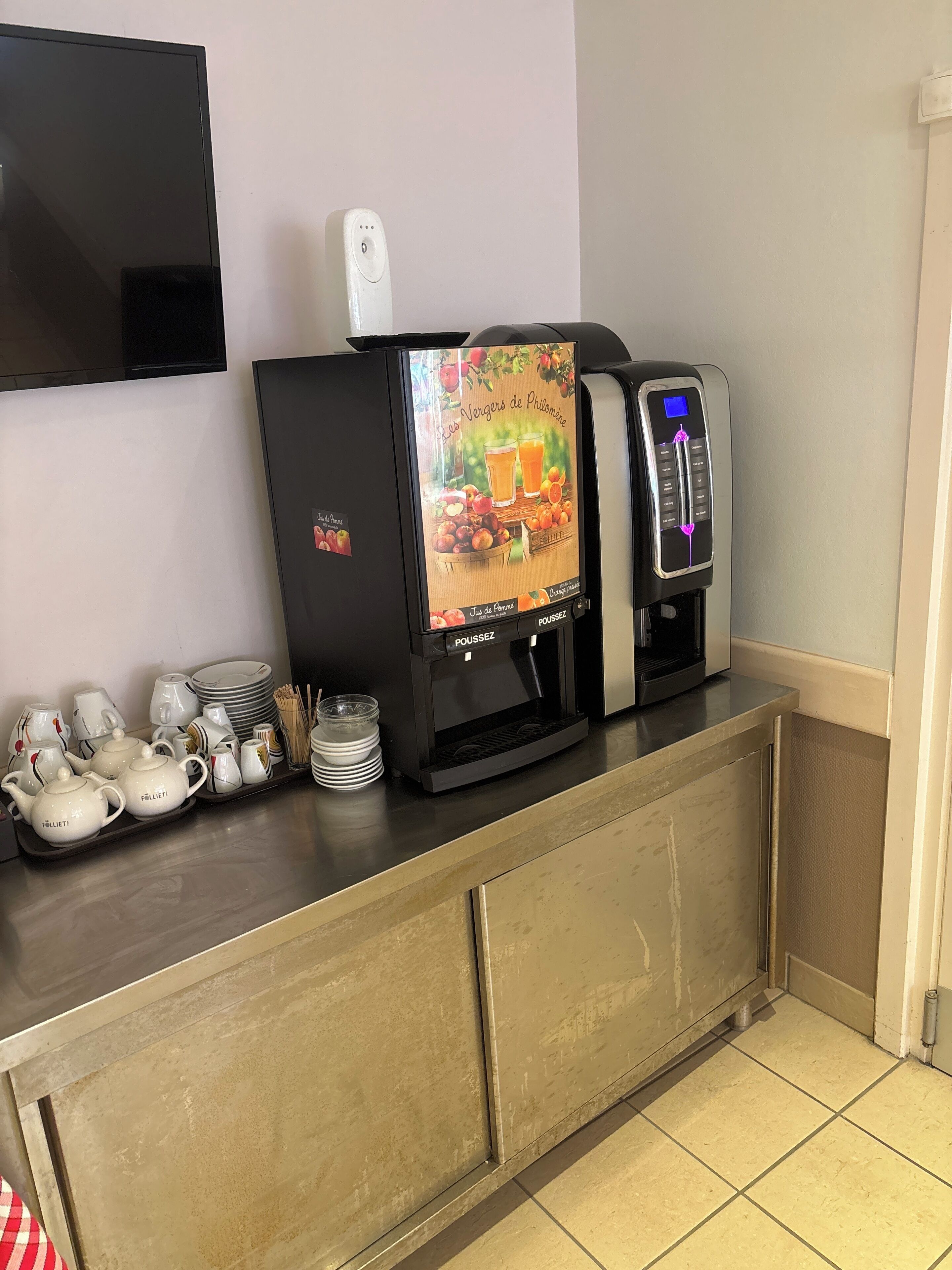 A coffee machine with a digital display, a tea set, and stacked plates on a counter.