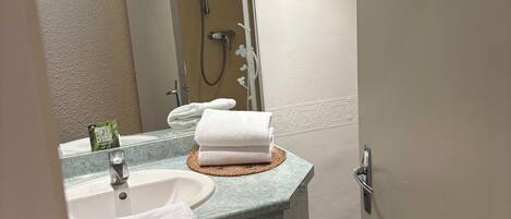 A bathroom with a sink, mirror, towel rack, and shower.
