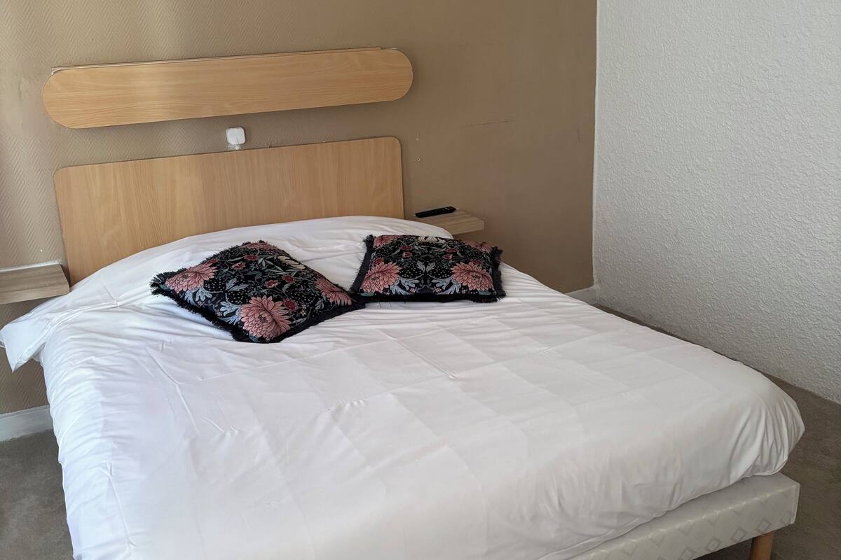 A bed with a wooden headboard, white bedding, and two floral-patterned pillows.