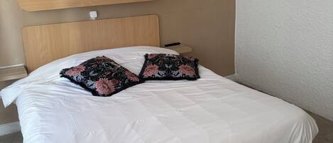 A bed with a wooden headboard, white bedding, and two floral-patterned pillows.