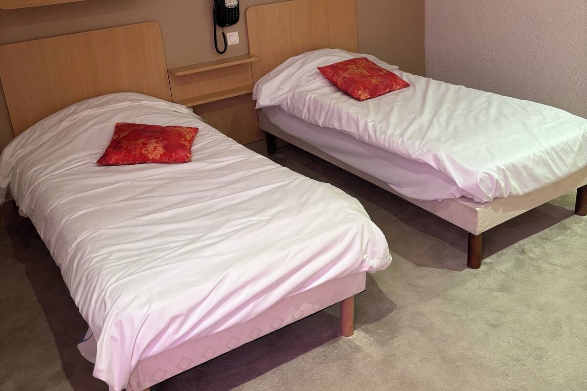 Two single beds with wooden headboards, a bedside phone, and a red pillow on each bed.