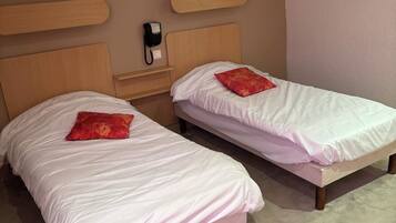 Dos camas individuales con cabeceros de madera, un teléfono en la mesita de noche y un cojín rojo en cada cama.