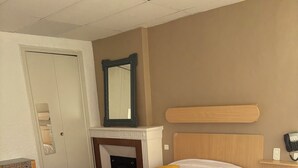Habitación de hotel con dos camas, cabecero de madera, espejo, teléfono y una mesita pequeña.