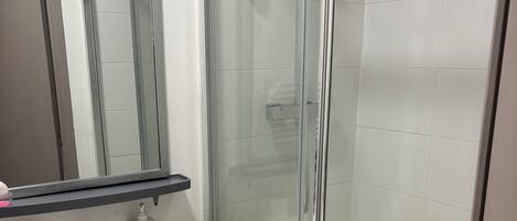 A bathroom with a glass shower enclosure, a white sink with a towel, and a mirror above the sink.