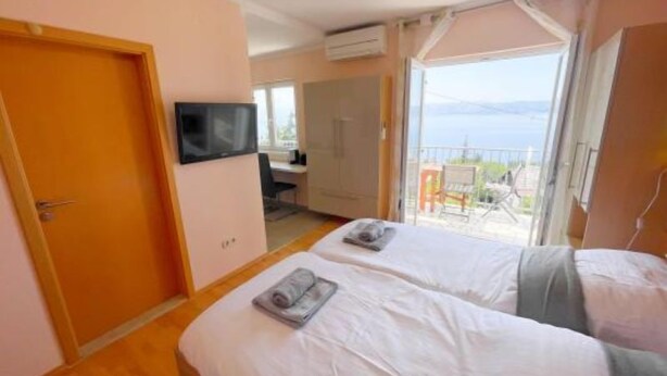 Quarto de hotel com duas camas, televisão, escrivaninha e varanda com vista para o mar.