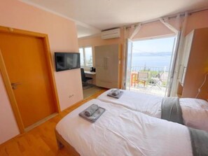 Habitación de hotel con dos camas, televisión, escritorio y balcón con vista al mar.