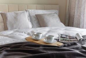 A neatly made bed with two white cups and saucers on a wooden tray, a rolled-up magazine, and a dark blanket. - Apartament Otyńska 4 - ProperUNIT (Wroclaw)