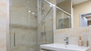 Een moderne badkamer met een douchecabine van glas, een witte wastafel met spiegel en wanden met een marmerprint.