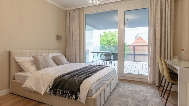 Een slaapkamer met een bed, een bureau en uitzicht op een balkon.