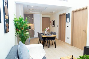 A modern living room with a sofa, a dining table with chairs, a potted plant, and a kitchen area in the background.