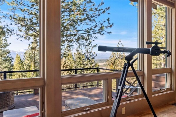 A telescope on a tripod by a large window overlooking a deck with a view of trees and mountains. - Mountaintop Cabin Hot Tub Views Family Golf (Portola)
