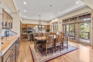A spacious kitchen with wooden cabinets, a dining area with a large table and chairs, and large windows offering a view of the outdoors. - Mountaintop Cabin Hot Tub Views Family Golf (Portola)