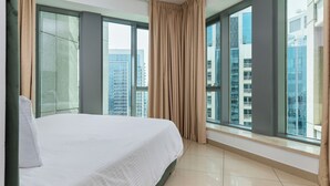 Une chambre d’hôtel dotée d’un grand lit, offrant une vue sur la ville grâce à de larges fenêtres du sol au plafond, et présentant un design moderne.