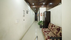 A hallway with a wooden ceiling, a potted plant, a sofa, and a refrigerator.