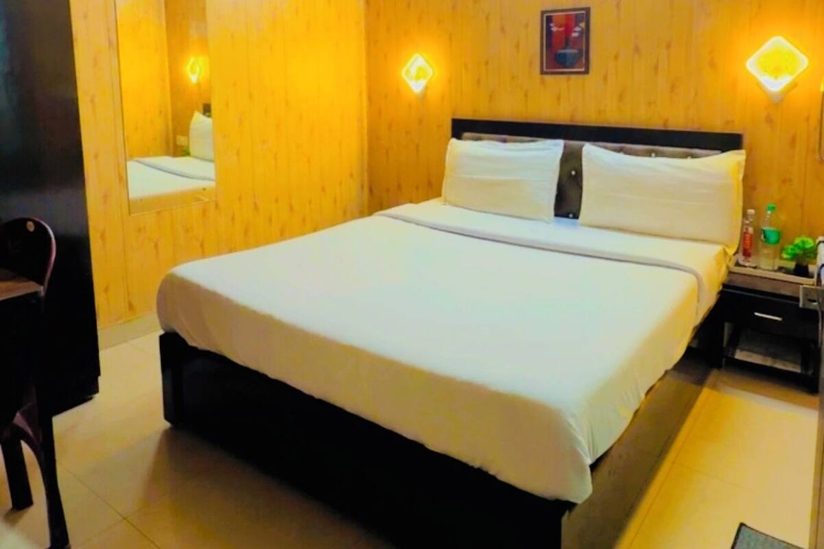 A hotel room with a wooden ceiling, a bed with white bedding, a ceiling fan, and wall-mounted lighting.