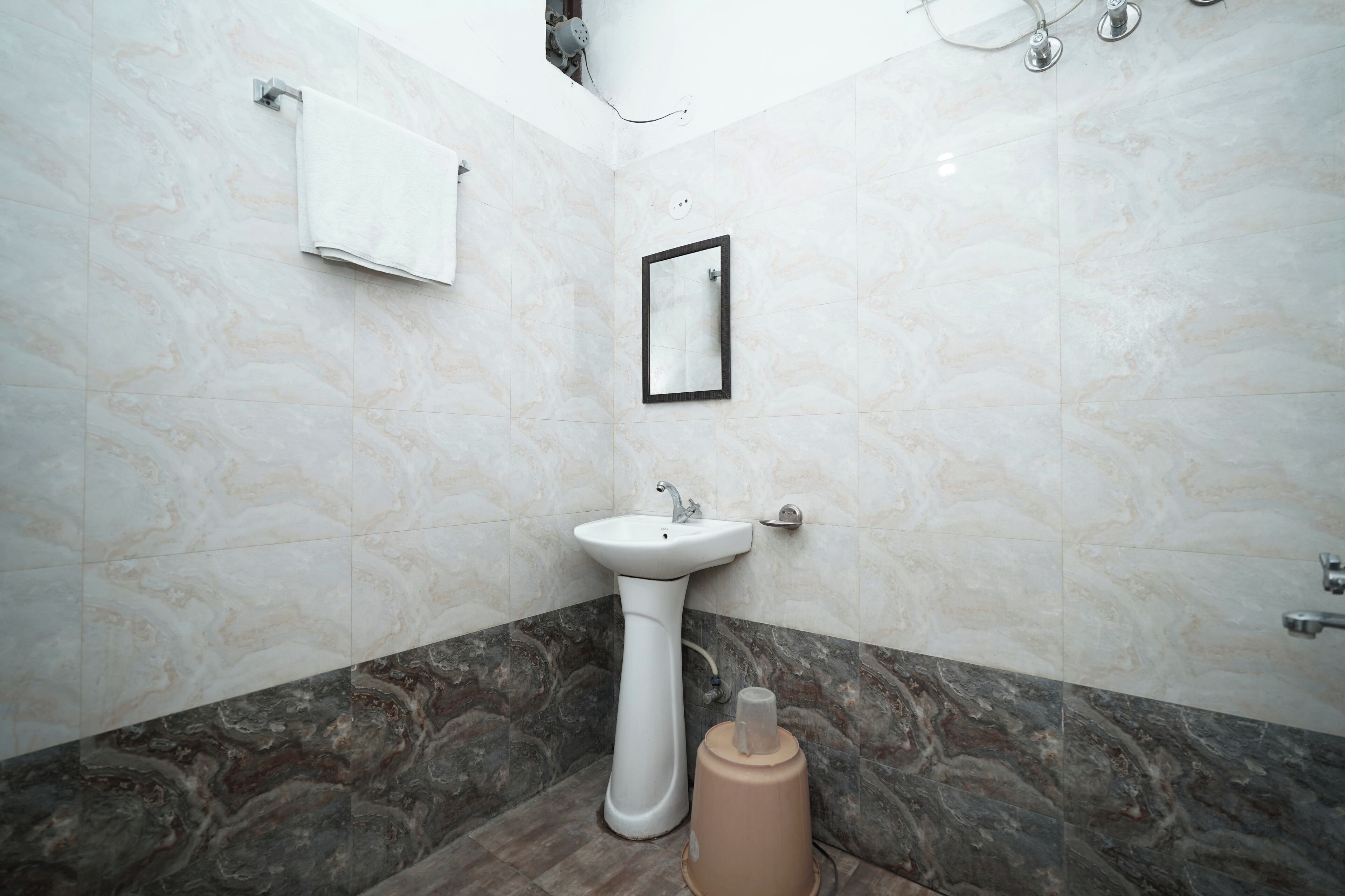 Un baño con lavamanos pedestal, espejo, toallero y pared con azulejos de mármol.