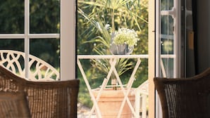 Une pièce dotée d'une grande fenêtre, de chaises en osier et d'une plante en pot sur un balcon.