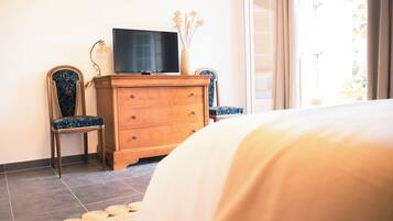 Une chambre à coucher avec un lit, une commode en bois, deux chaises, un téléviseur et une fenêtre avec des rideaux.