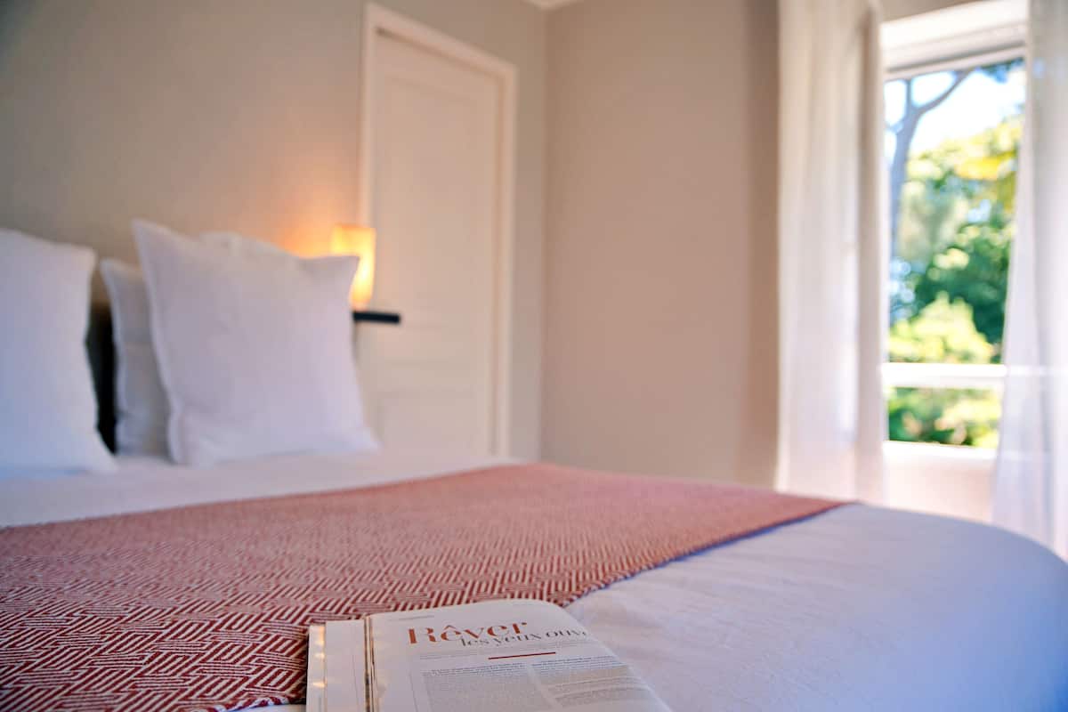 A neatly made bed with a red and white patterned bedspread, a white pillow, and a book titled "Réver" on the bed.