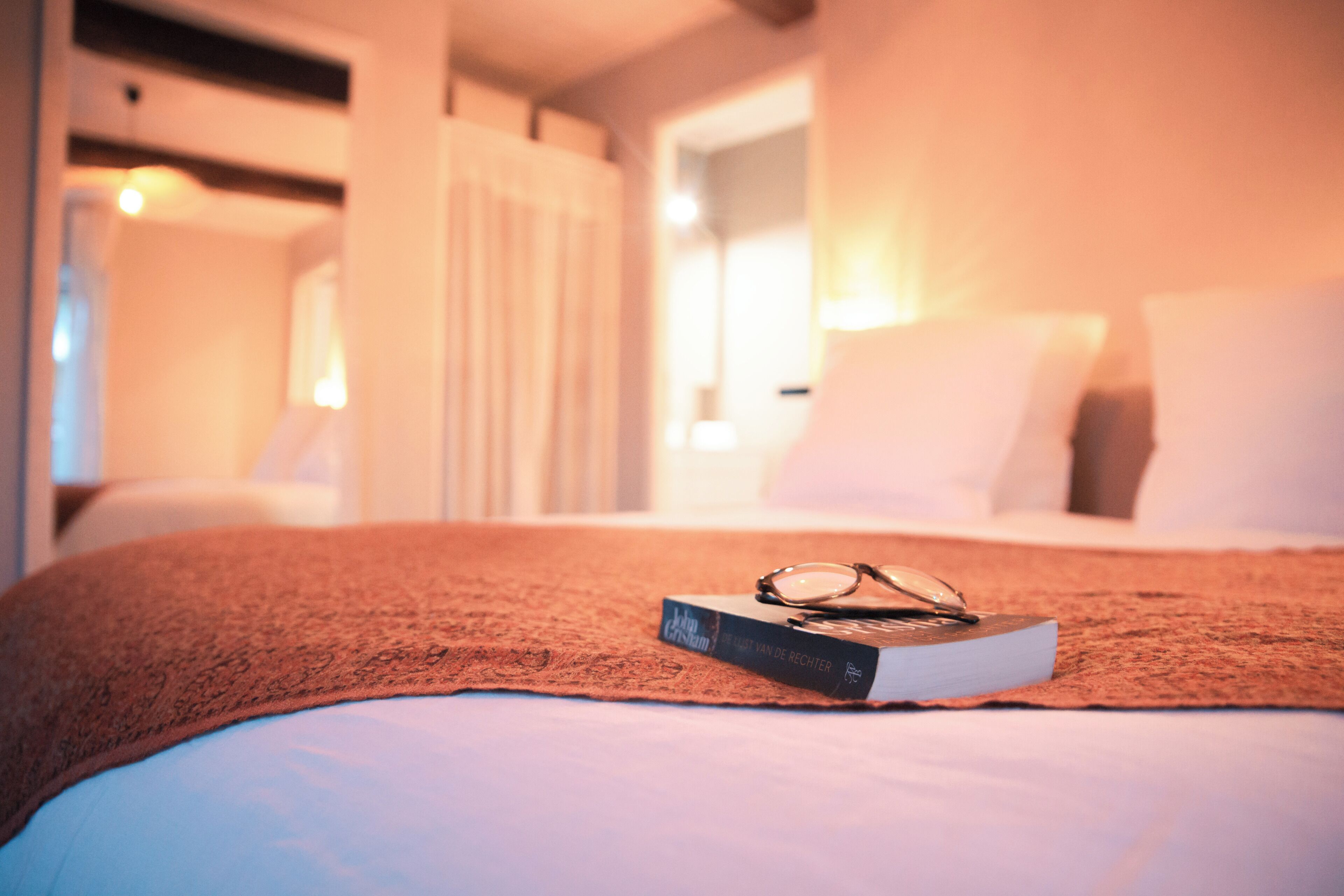 Un lit bien fait, avec une couverture marron, un livre et une paire de lunettes posés dessus.
