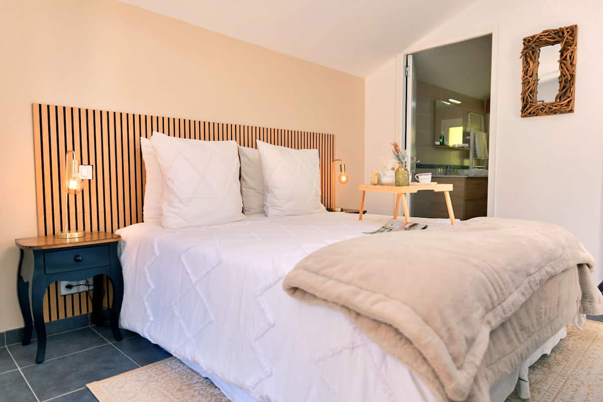 A neatly arranged bedroom with a bed, bedside table, lamp, and a mirror on the wall.