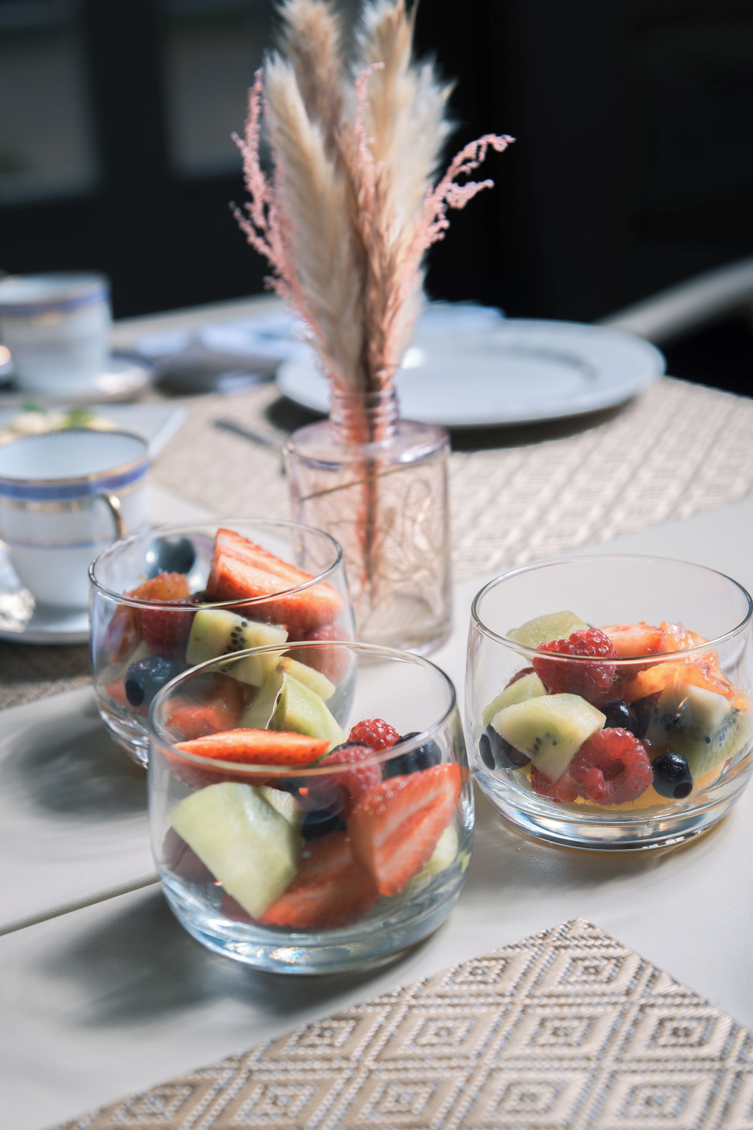 Tres vasos de vidrio transparentes llenos de fruta variada sobre una mesa.
