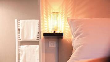 A hotel room with a bed, a bedside lamp, a towel rack, and a wooden floor.