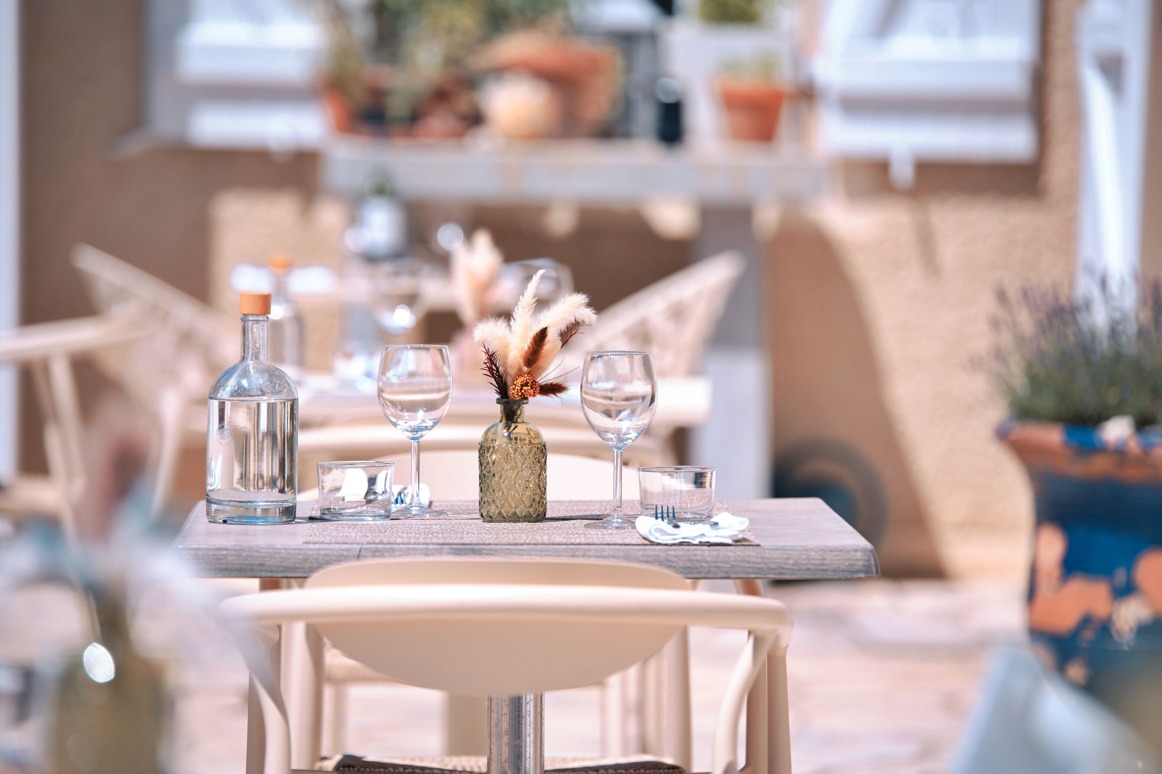 A dining table set with clear glass bottles, wine glasses, and a decorative vase with dried flowers.