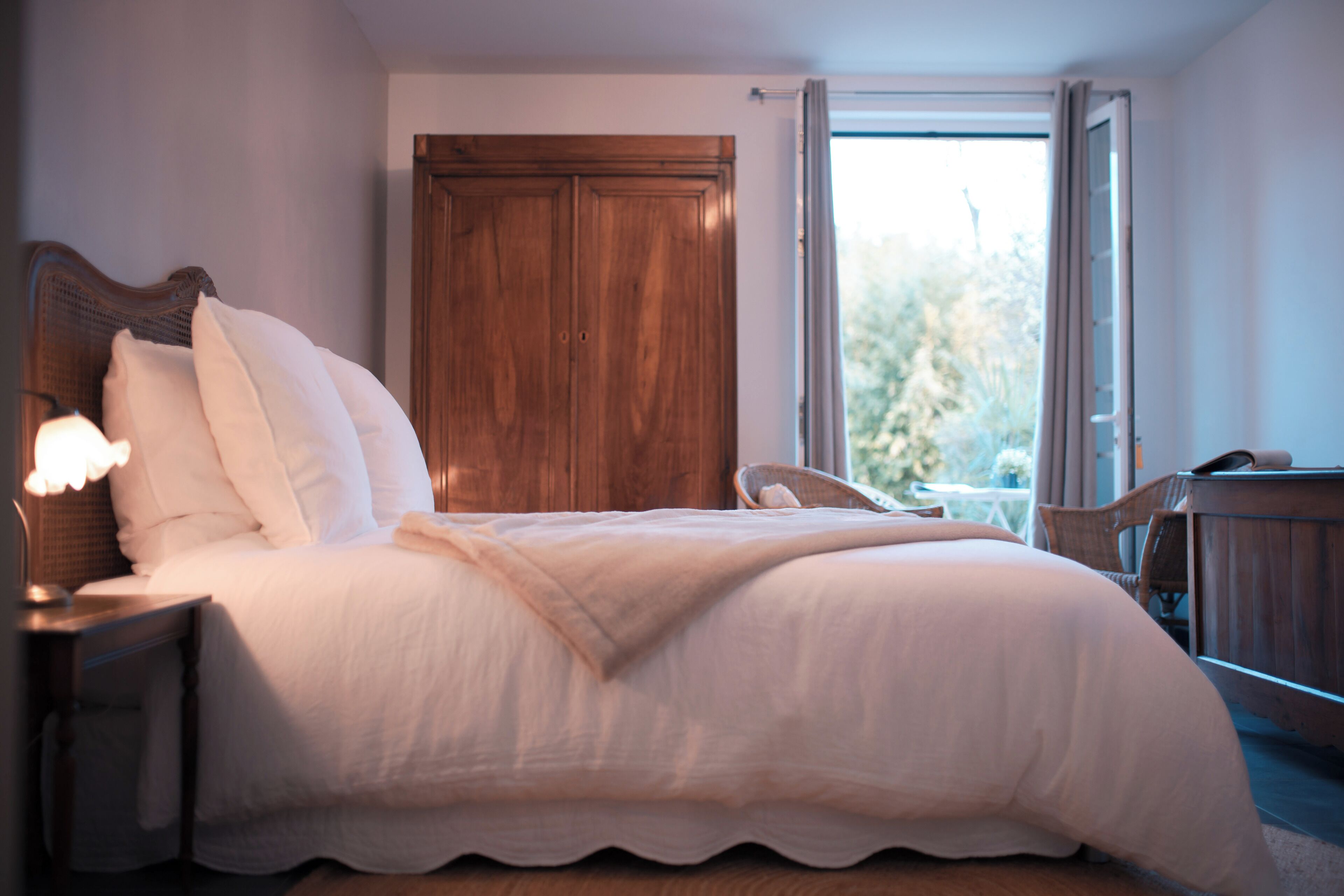 Un lit bien fait, avec du linge de lit blanc, une tête de lit en bois et une table de chevet avec une lampe.