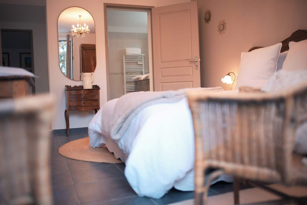 A bedroom with a bed, a bedside table, a mirror, a chandelier, and a wardrobe.