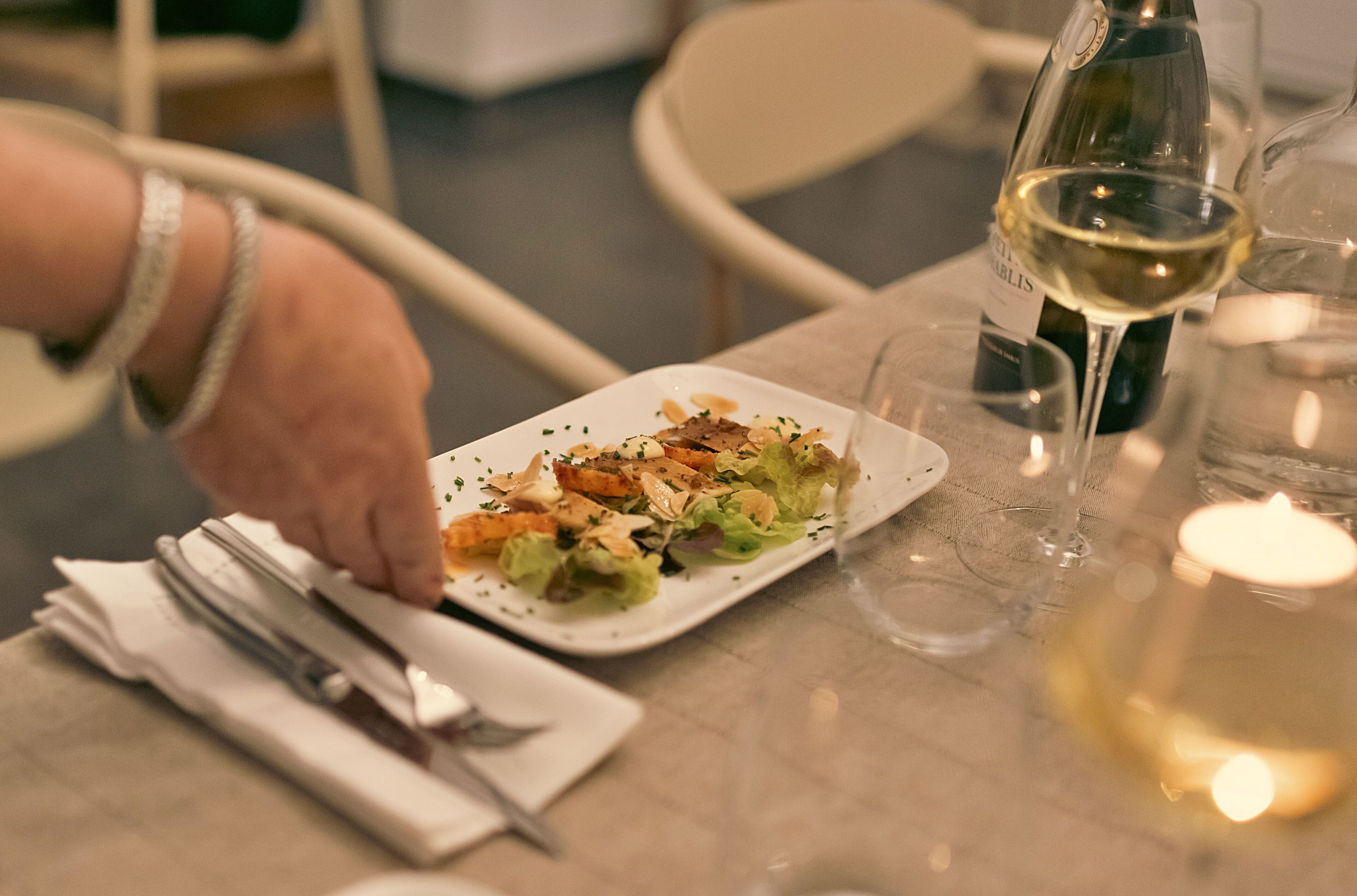 Une table à manger avec une assiette de nourriture, une bouteille de vin et des verres.