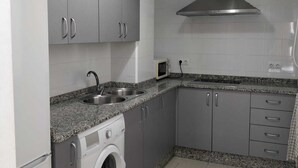 Une cuisine compacte avec des meubles gris, un évier en acier inoxydable, un four à micro-ondes, un lave-linge et un luminaire suspendu rouge.