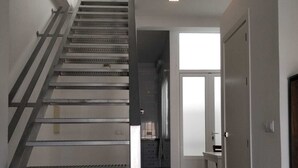 Un intérieur moderne avec un escalier menant à un deuxième étage, un couloir avec une porte et une fenêtre qui laisse entrer la lumière naturelle.