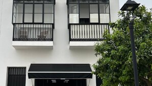 Un bâtiment à deux étages, doté d’une façade blanche, de volets noirs et d’un auvent noir au-dessus de l’entrée.