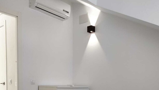 Une chambre d’hôtel comprenant un lit, une table de chevet, un climatiseur fixé au mur et un luminaire fixé au mur.