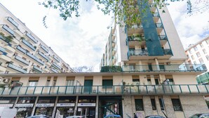 A multi-story building with balconies, a storefront with signs, and parked cars. - VivimiHome-Apartment near Milano Central (Milan)