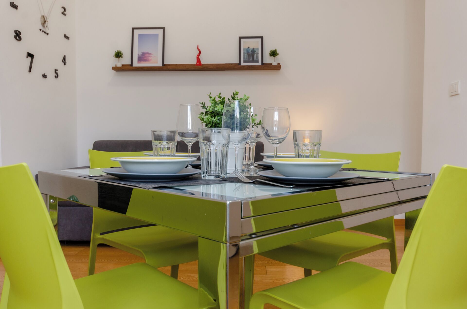 Una mesa de comedor con dos sillas, superficie de vidrio y un juego de platos y vasos.