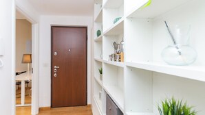 A hallway with a wooden door, white shelving with kitchen utensils, and a potted plant. - VivimiHome-Apartment near Milano Central (Milan)
