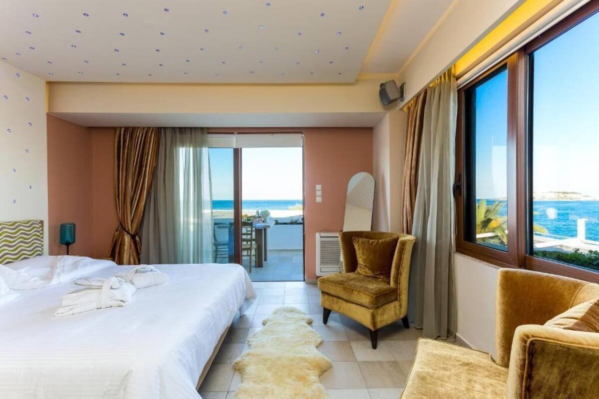 A hotel room with a bed, a chair, a view of the sea, and a balcony.
