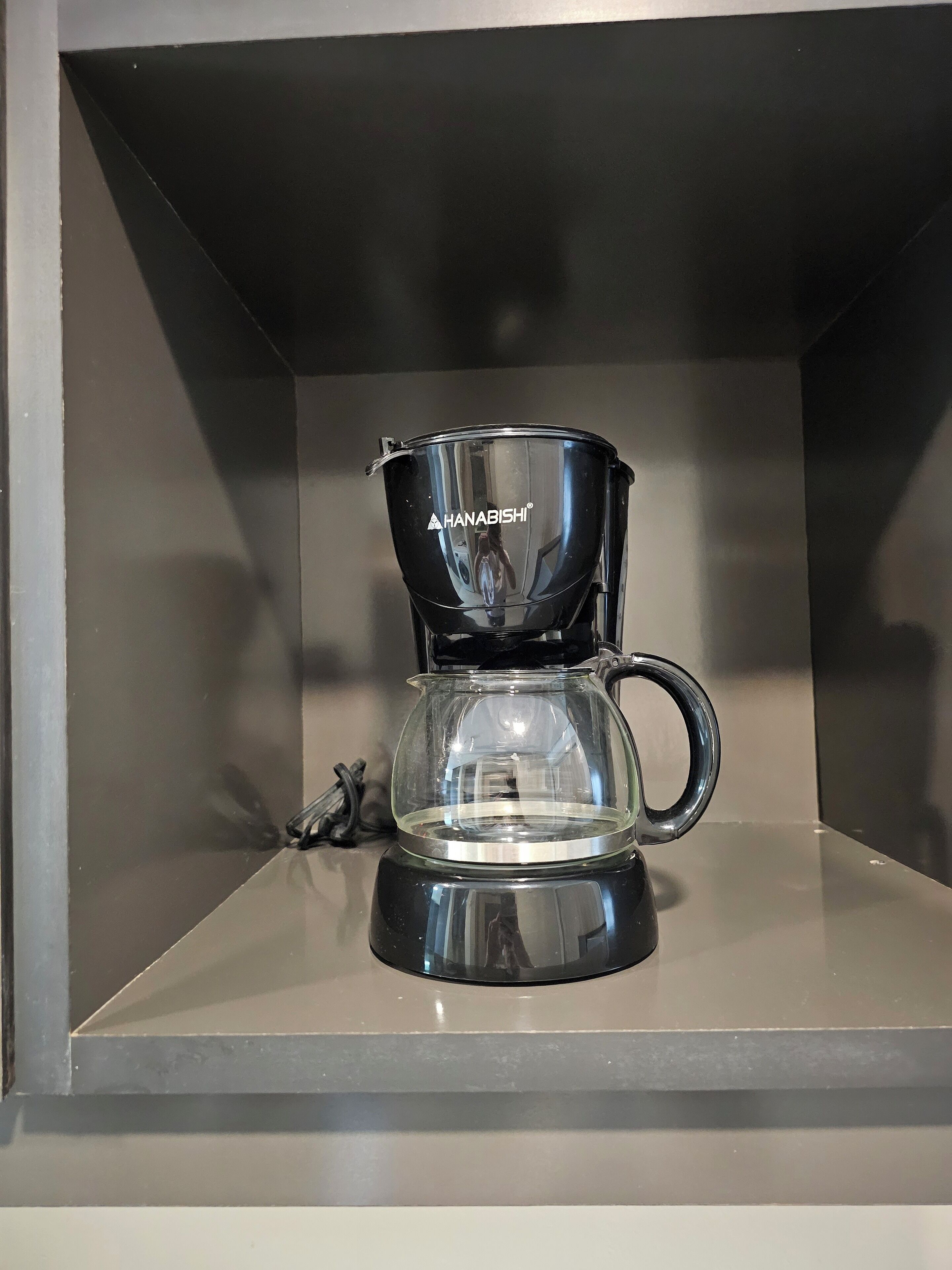 A black HANABISHI coffee maker on a shelf.