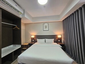 A hotel room with a large bed, two bedside lamps, a headboard, a wall-mounted air conditioner, a coat rack, and a framed picture on the wall. - The Residences at BCCT by Stays PH (Taguig)