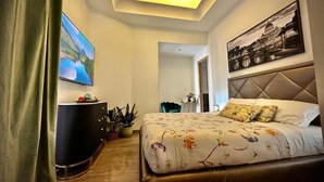 A modern hotel room with a large bed, a flat-screen TV, a dark-colored dresser, and a painting on the wall.